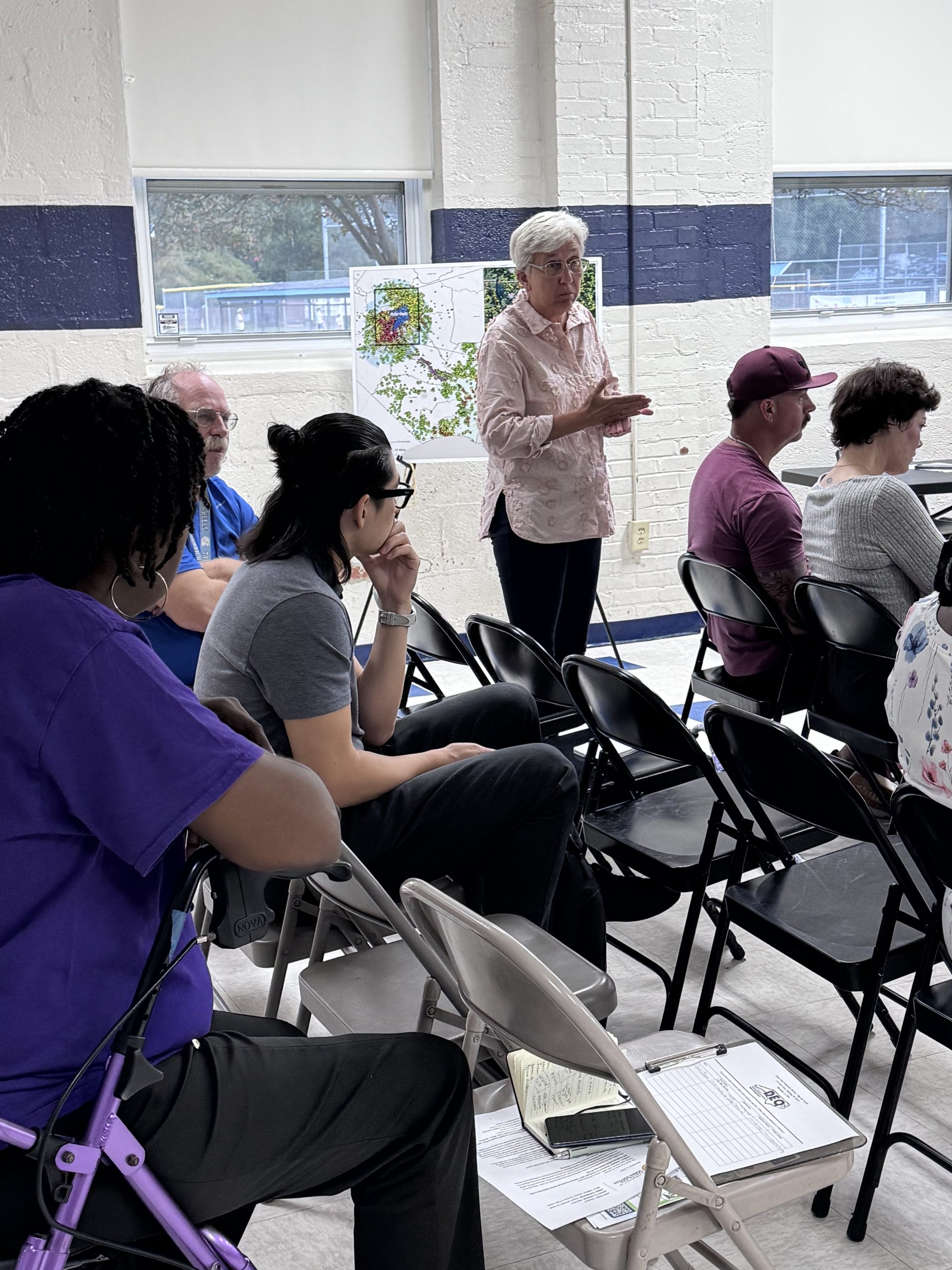 Cedar Creek resident Vickie Mullins stands and gestures while responding during a Sept. 15 community meeting at the Stedman Recreation Center. Residents sit in folding chairs around her, and a map is displayed on an easel behind her.