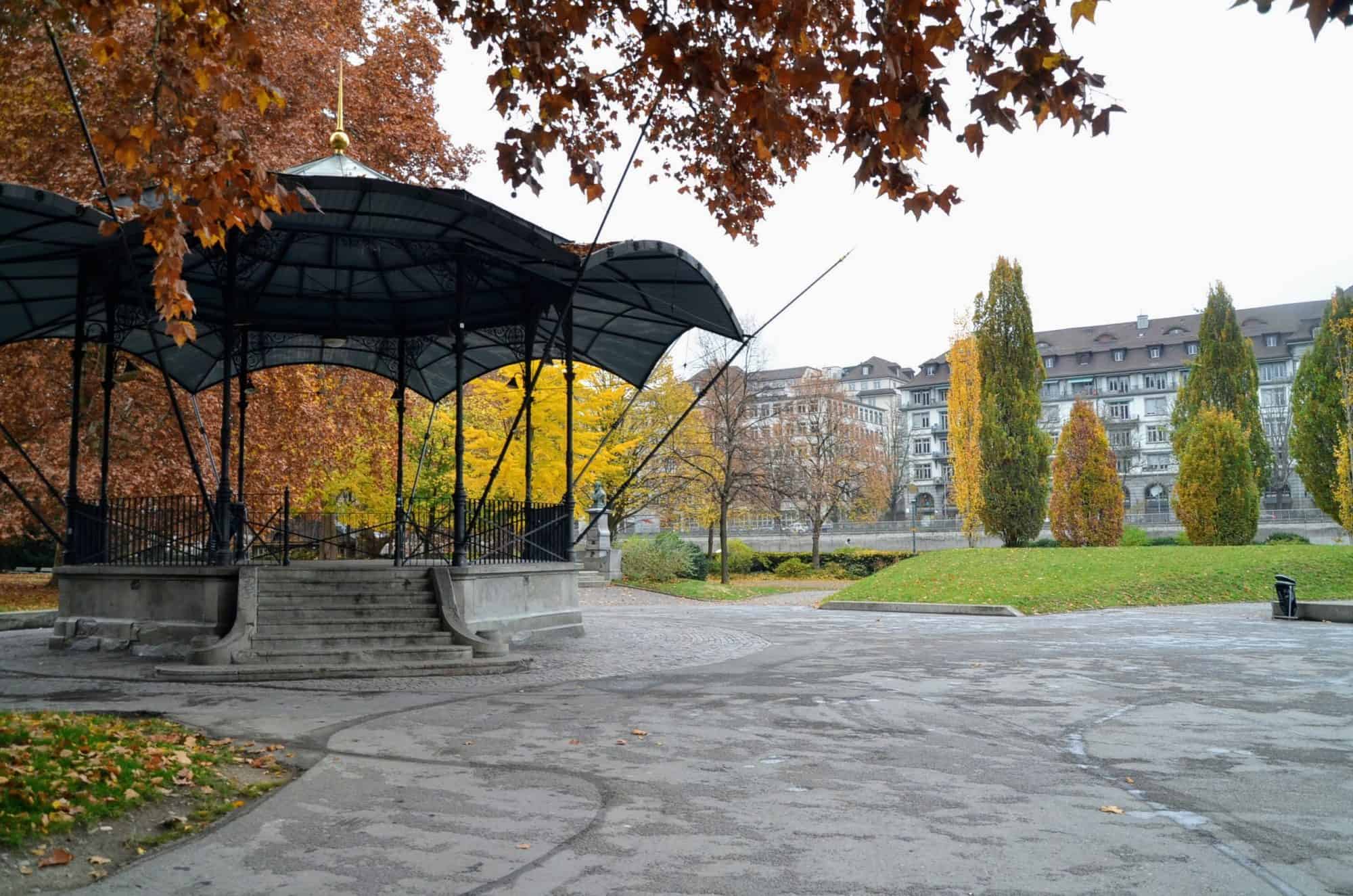 A gazebo in a park with fall colored trees
