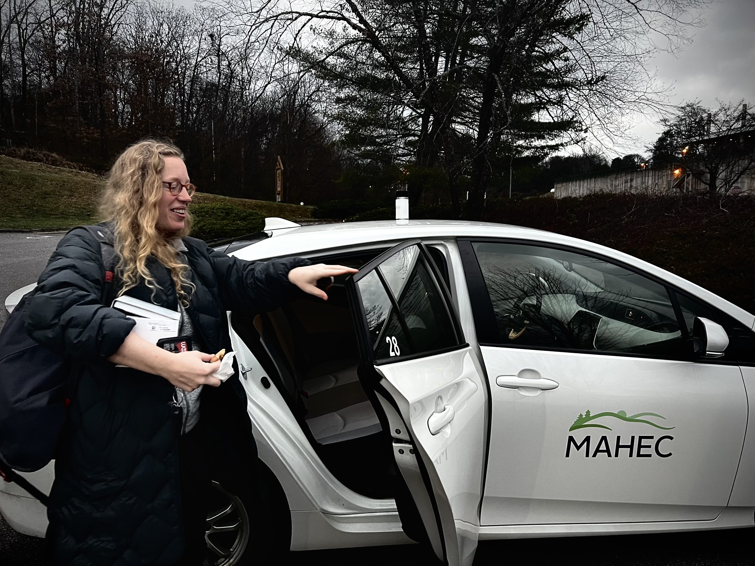 a woman with blonde curly hair and glasses closes the door to a white car with MAHEC on the side. MAHEC tries to fill the labor and delivery gap in the county