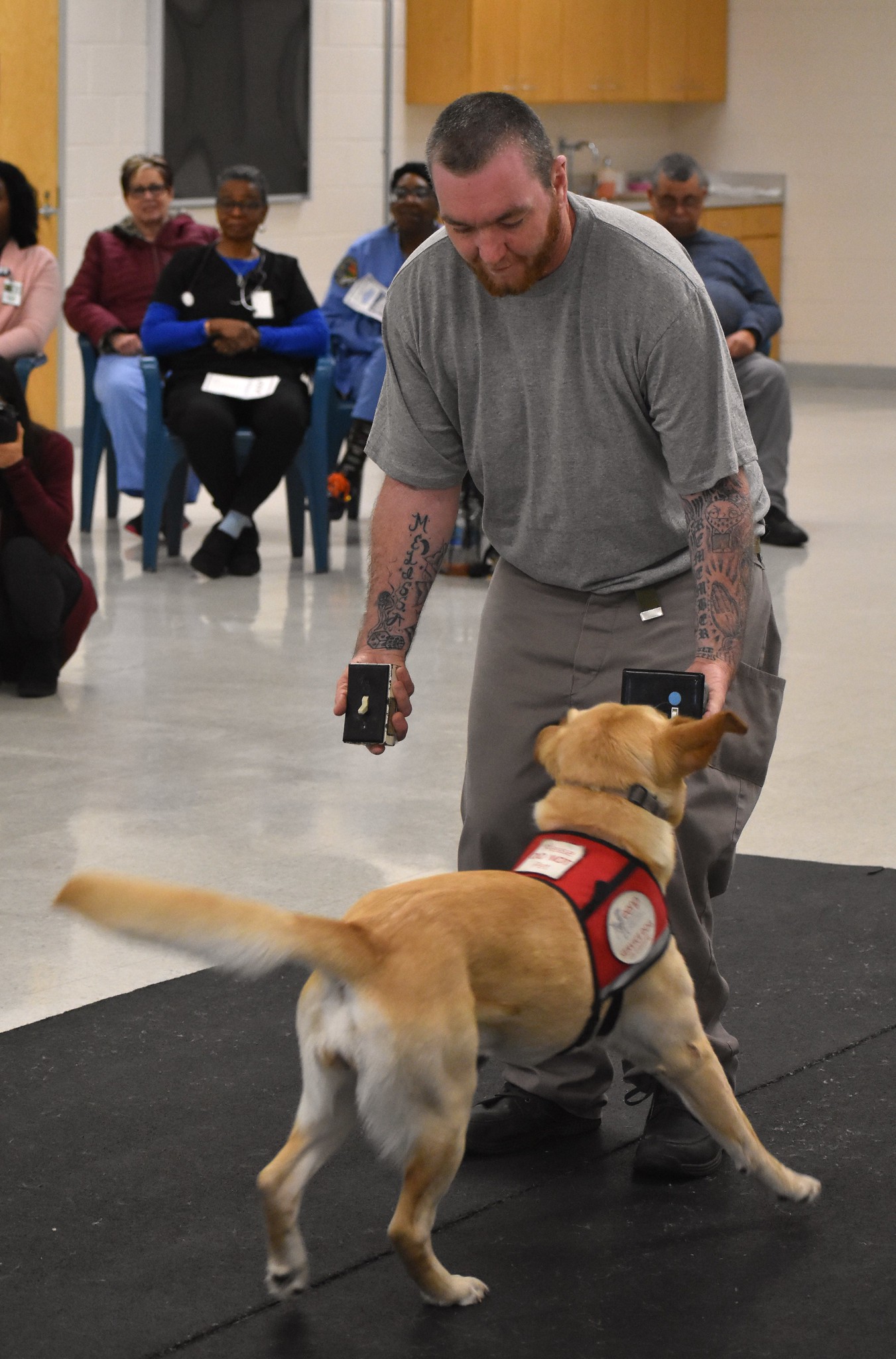 A trainer holds two light switches as he instructs a service dog on which to turn on.
