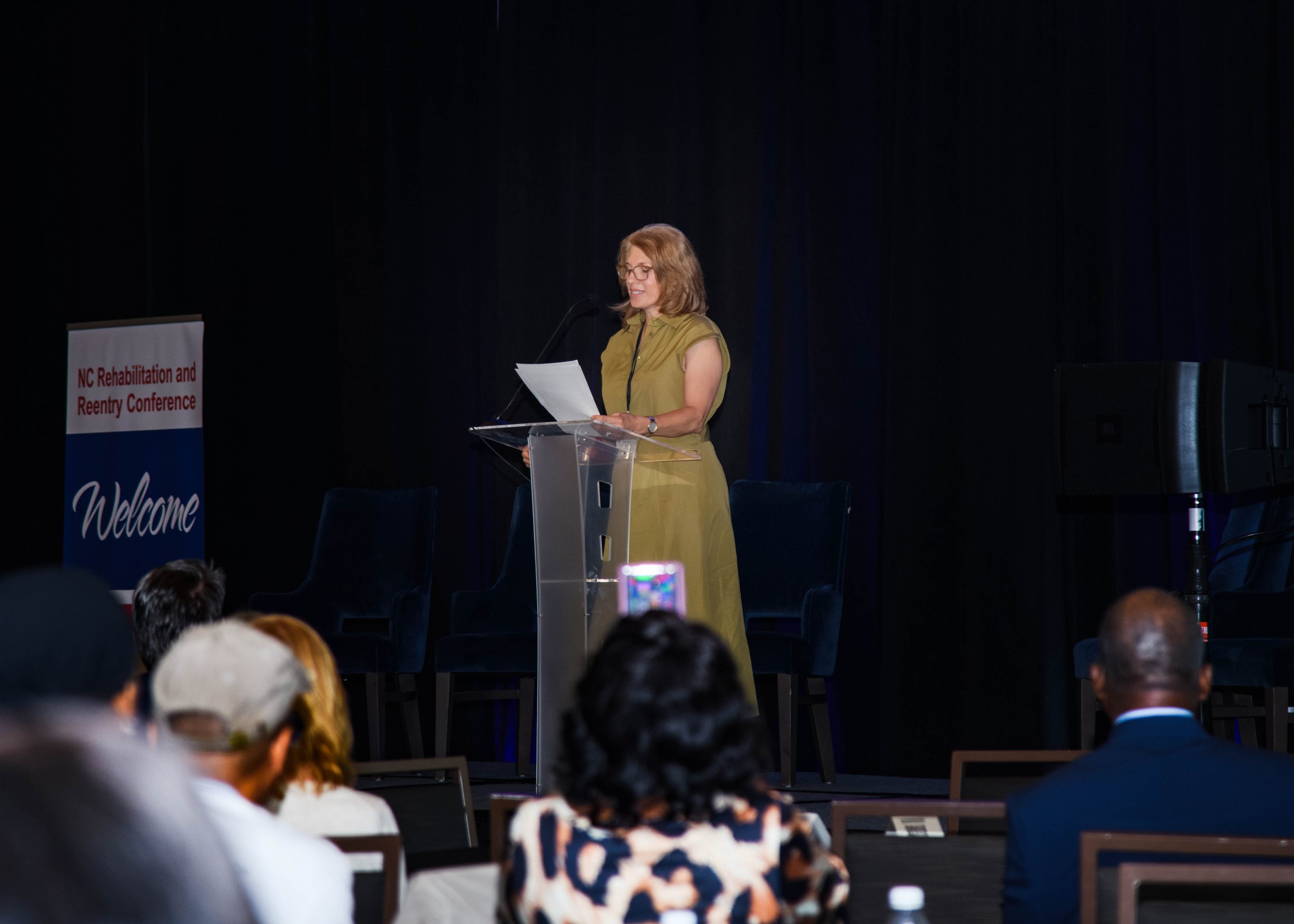 A woman in a dress speaks at a podium during the NC Rehabilitation and Reentry Conference talking about her focus on supporting reentry