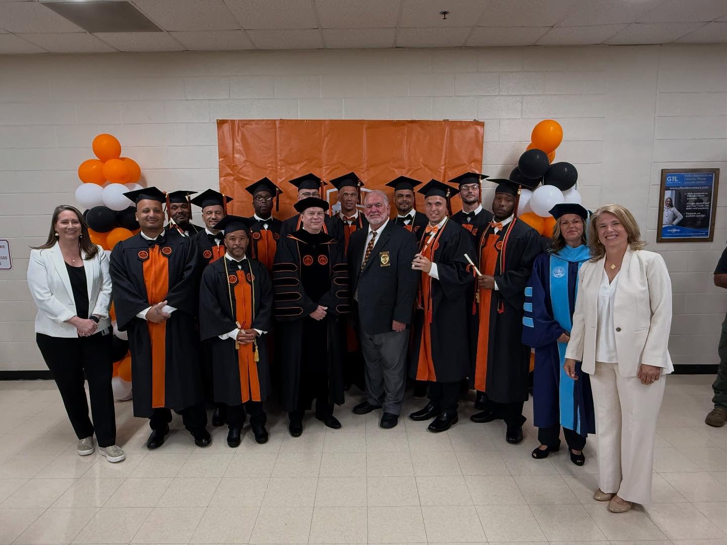 A group of incarcerated men in graduation caps and gowns pose for a photo