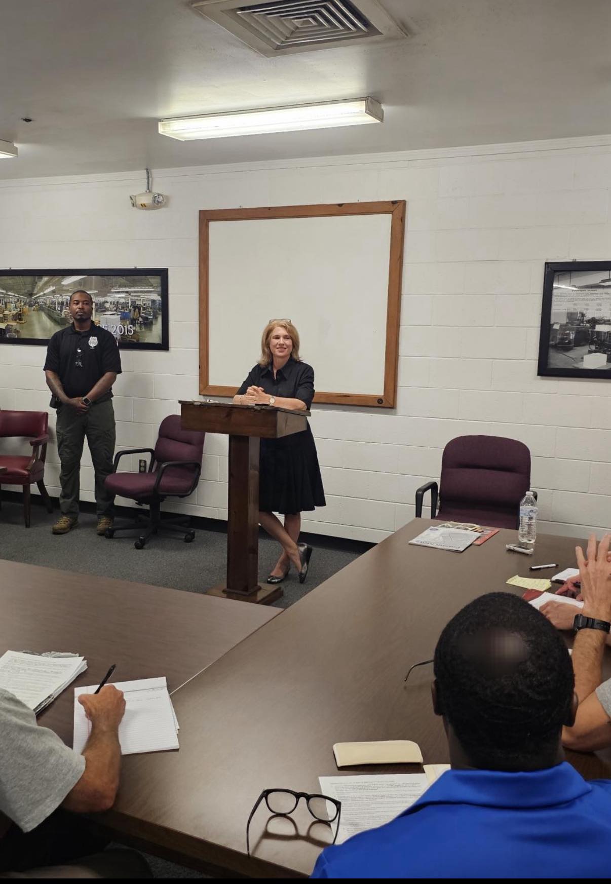 A woman stands a a podium answering questions from incarcerated writers seated around her
