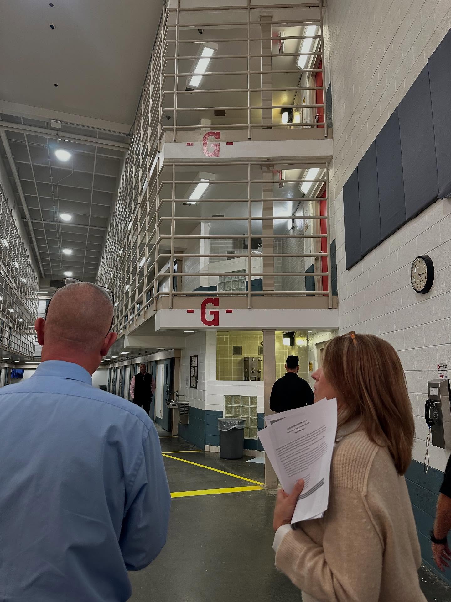 A woman holds paper while touring a prison with a warden standing beside her