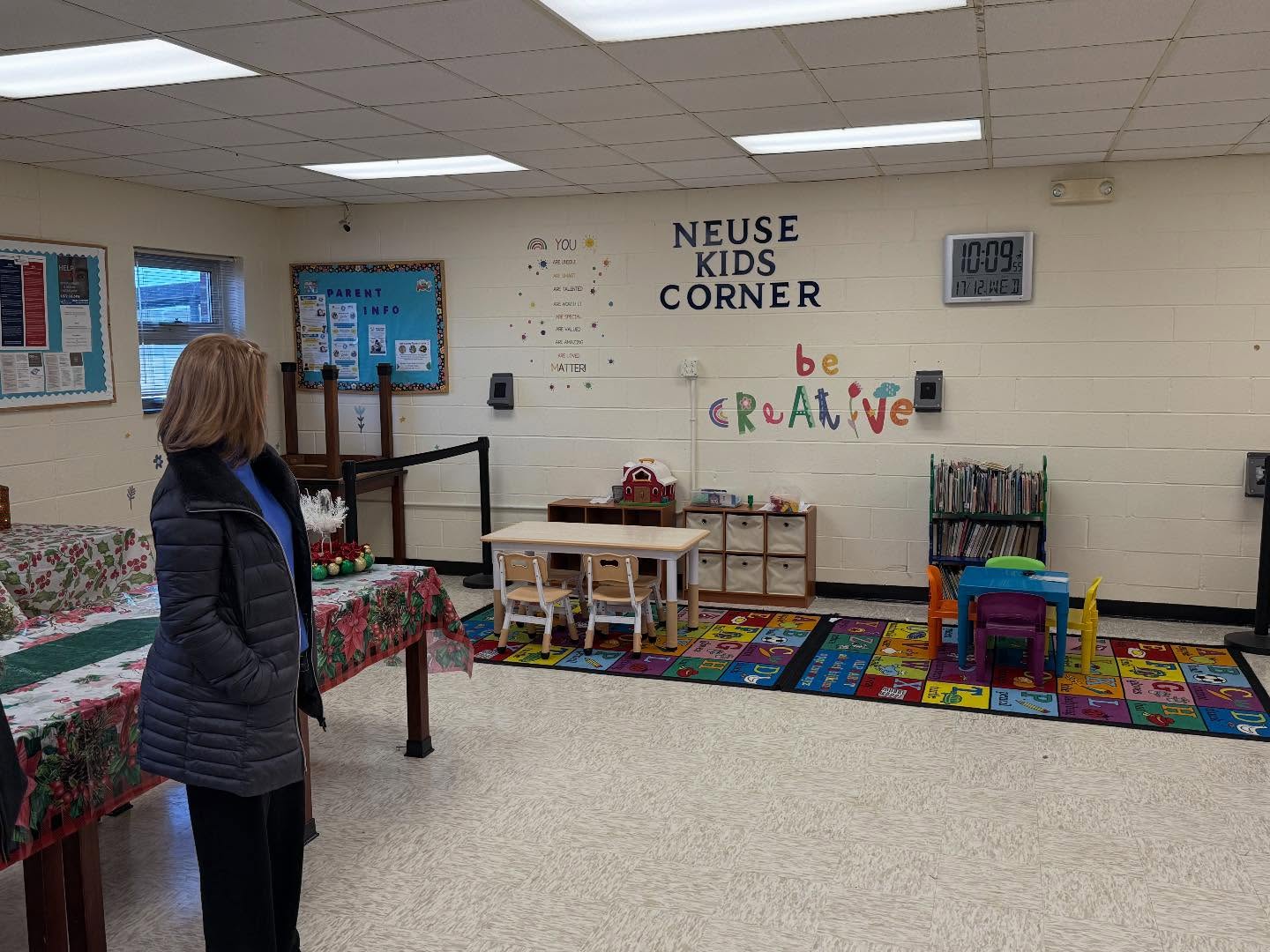 A white woman stands inside a prison visitation room that has a kids corner with small tables and games