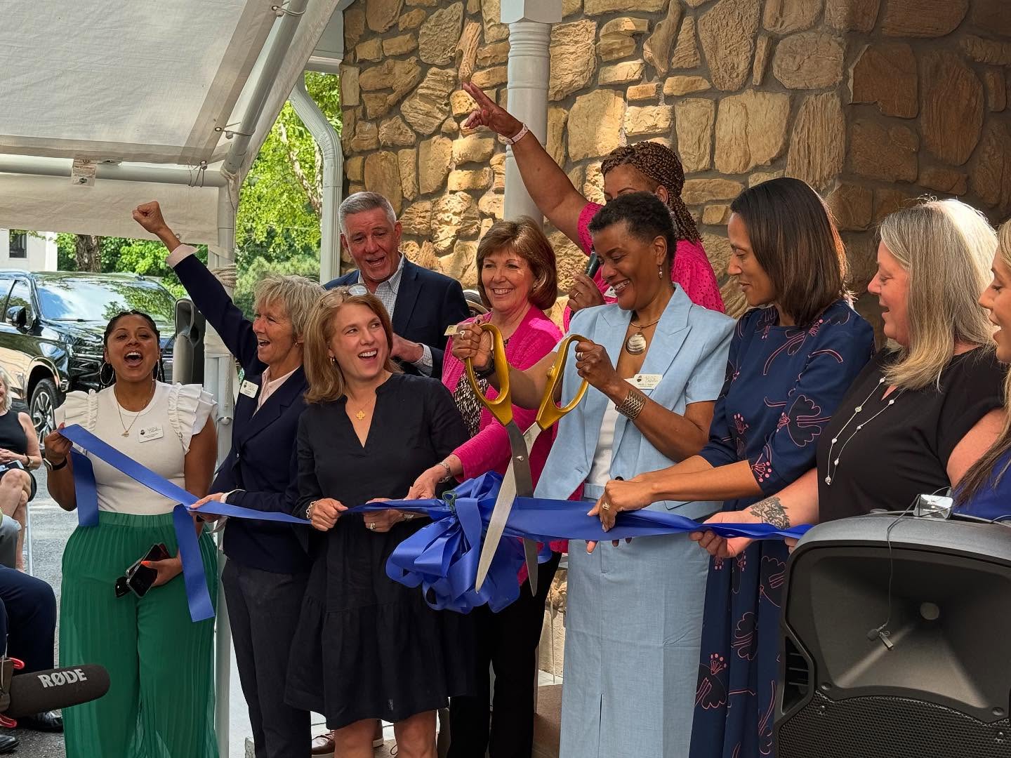 A group of people stand in front of a blue ribbon as it is cut with big scissors to mark the opening of a new program center to support justice-involved women