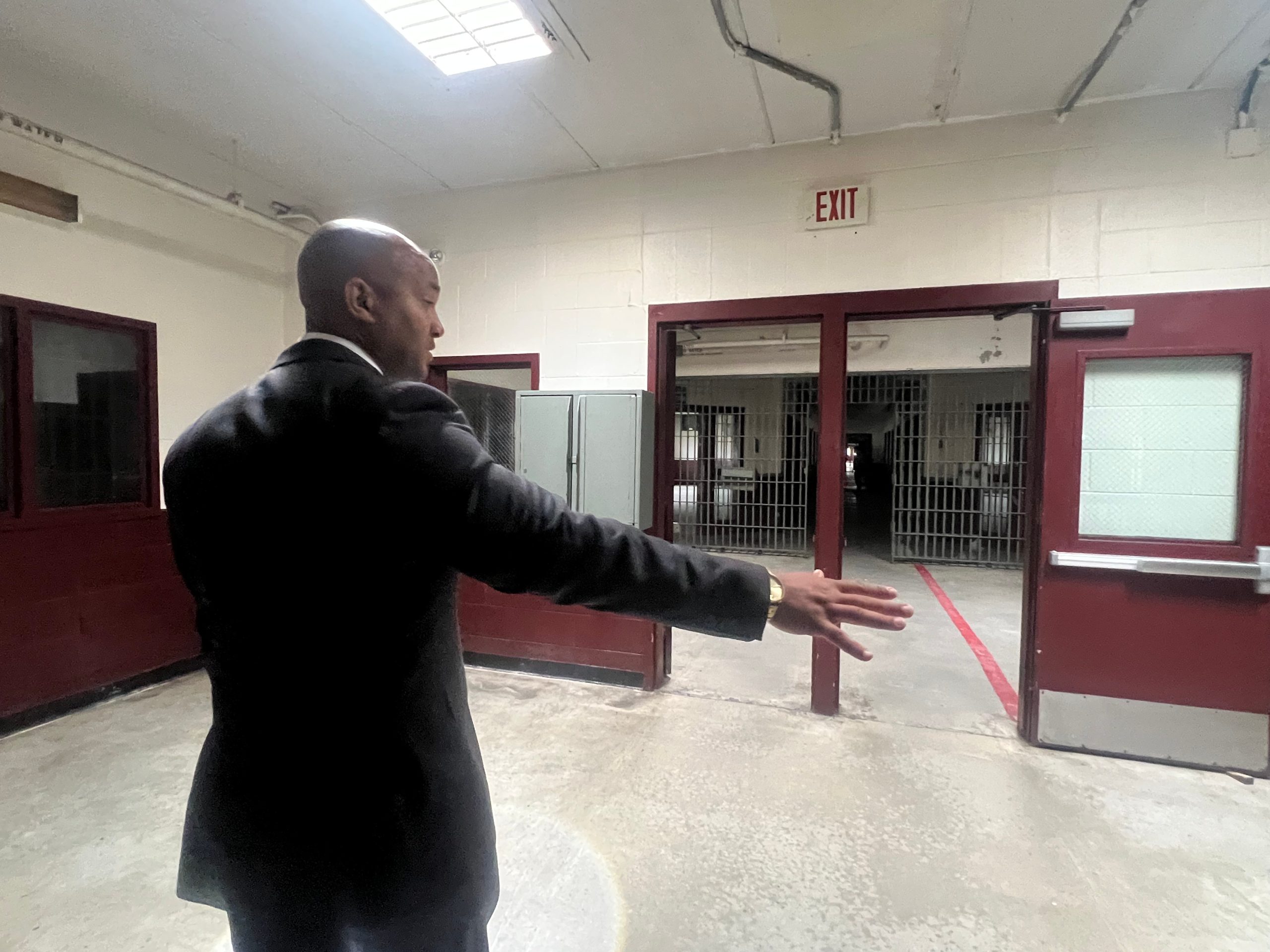 A man in a suit stands in a former prison, motioning with his hands at various features and describing his renovation plans