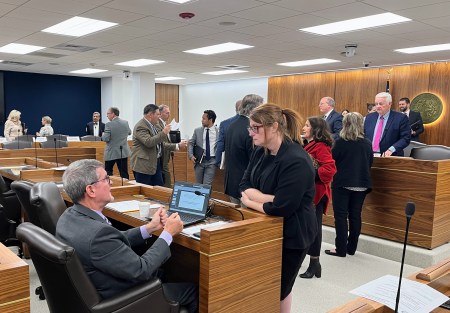 Kelly Crosbie and Rep. Carson Smith talk in a legislative committee room with people mingling behind them