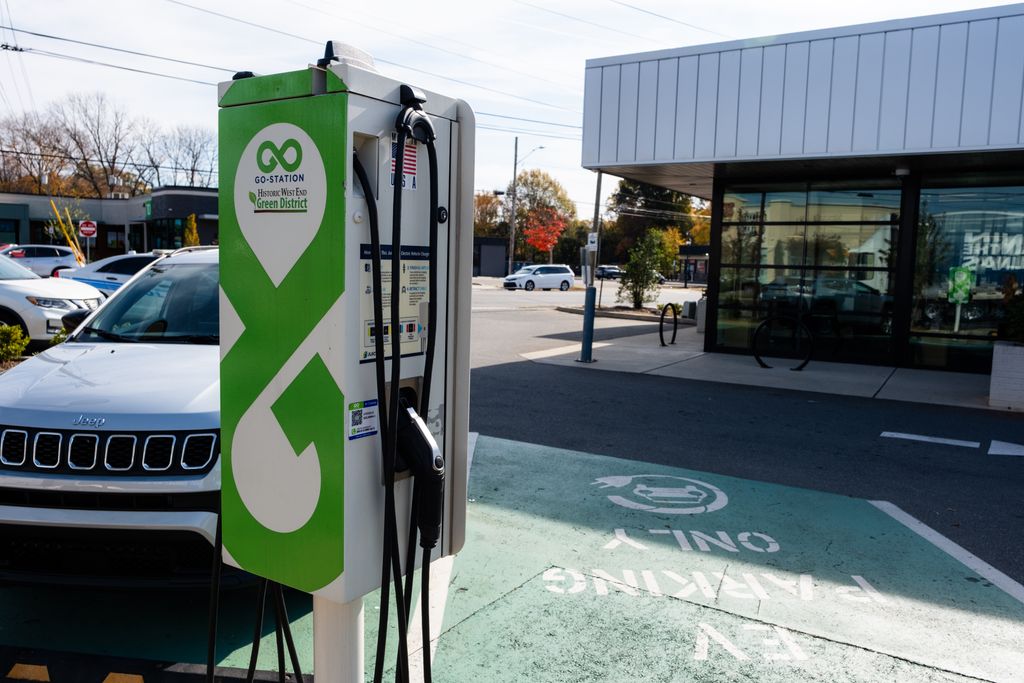 A single electric vehicle charging station in front of a green parking space painted with the words ‘EV Parking Only’ and a white car-and-cord symbol, in Charlotte’s Historic West End Green District.