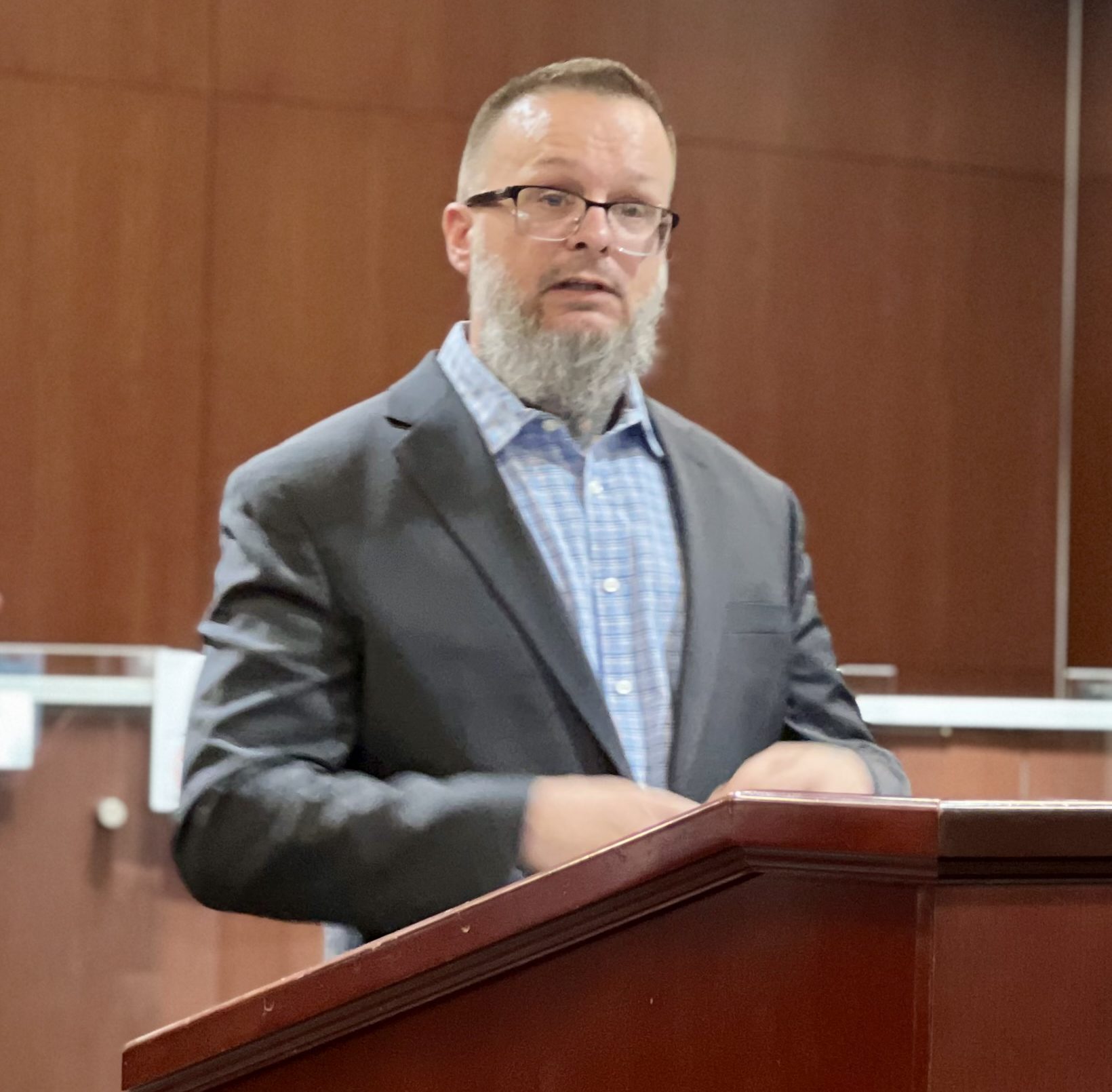 A white man in a suit stands at a podium talking about LEAD programs and their benefits