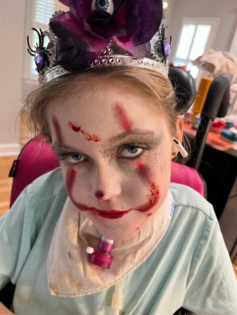 Shows a little girl with pale foundation makeup and red streaks on her face looking straight at the camera. Having home care help allows her to participate in trick or treating