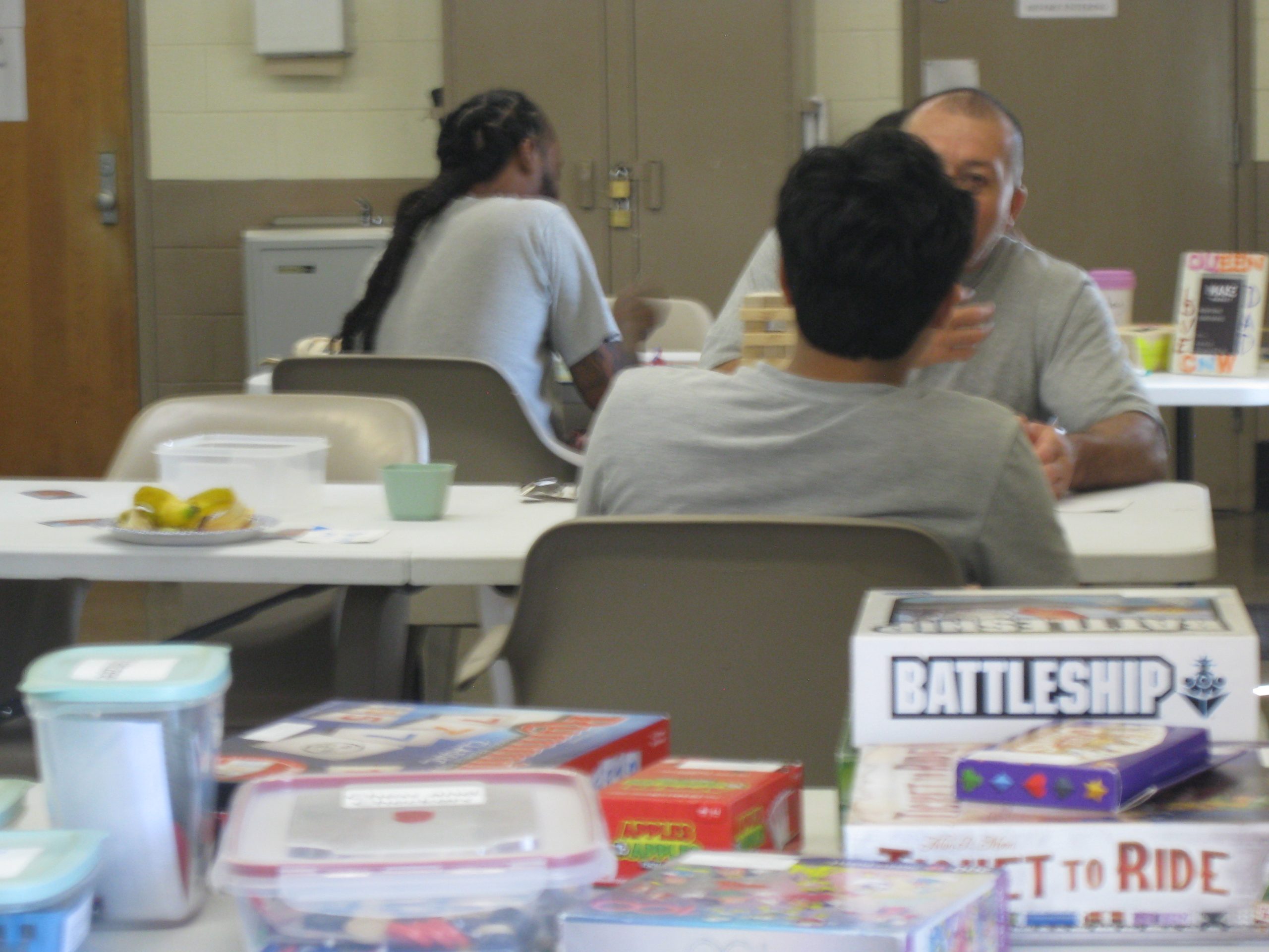 Several fathers and children sit around tables talking. Their backs are to the camera. A table of board games is in the foreground.