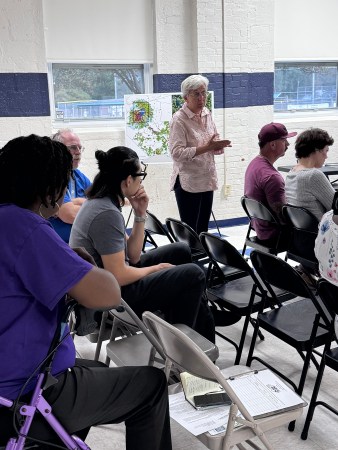Cedar Creek resident Vickie Mullins stands and gestures while responding during a Sept. 15 community meeting at the Stedman Recreation Center. Residents sit in folding chairs around her, and a map is displayed on an easel behind her.