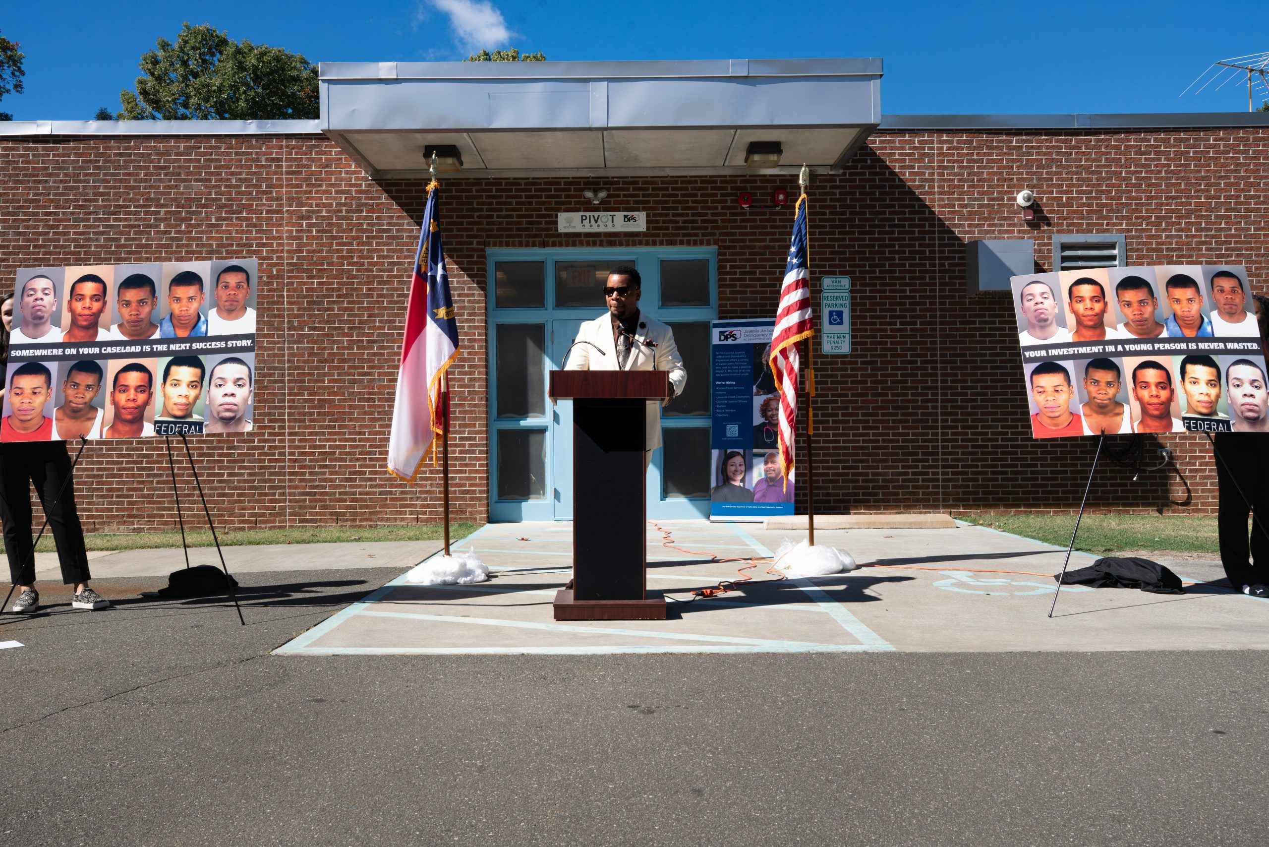 A black man stands at a podium flanked by posters of his mugshots