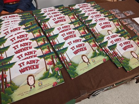 A table is filled with rows of a children's book titled "It Ain't Nothin'" about resilience at a conference for kinship caregivers.
